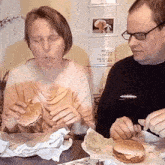 a man and a woman are eating hamburgers at a table with a sign on the wall that says " i love you "