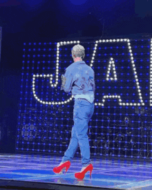 a man in a denim jacket is dancing on a stage in front of a sign that says ' a ' .