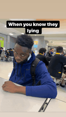 a man wearing a blue nike jacket sits at a table in a cafeteria