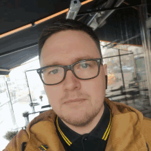 a man wearing glasses and a yellow jacket takes a selfie outside