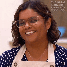 a woman wearing glasses and an apron is smiling in front of a sign that says the great canadian baking show