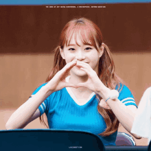 a girl in a blue shirt making a heart shape