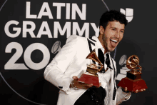 a man is holding two latin grammy awards