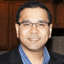 a man wearing glasses and a blue striped shirt is smiling for the camera