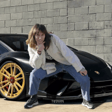 a woman kneeling down in front of a black car with gold wheels