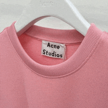 a pink acne studios t-shirt is hanging on a white hanger