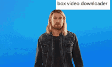 a man with long hair and a beard is standing in front of a blue background with a box video downloader written above him