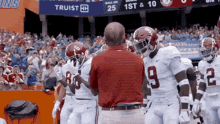 a man in a red shirt with the number 9 on his shirt talks to a group of football players