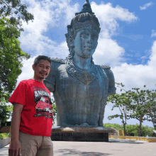 a man standing in front of a statue wearing a red shirt that says angry