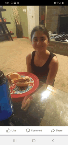 a girl is sitting at a table with a plate of hot dogs and a water bottle