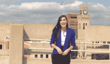 a woman in a blue jacket is standing in front of a building with a clock tower in the background