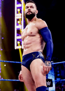 a shirtless wrestler stands in a wrestling ring with the letter w on the wall behind him