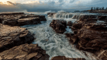 waves crashing on a rocky shoreline with trees in the distance