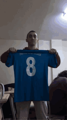 a young man is holding up a blue shirt with the number 8 on it