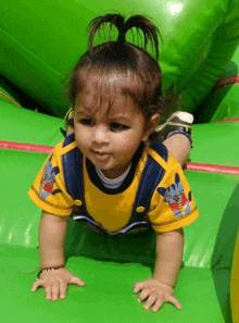 a baby in a yellow shirt with a cat on it is crawling on a green surface