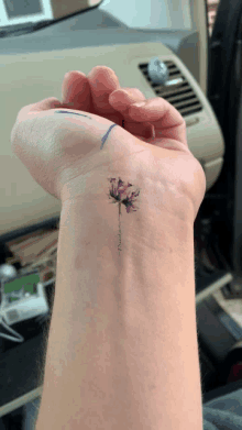 a woman 's wrist has a small tattoo of a purple flower with the name sandra on it