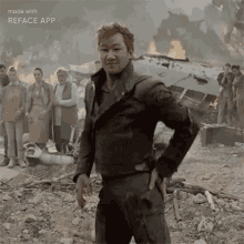 a man in a leather jacket is standing in front of a group of people in a ruined city .