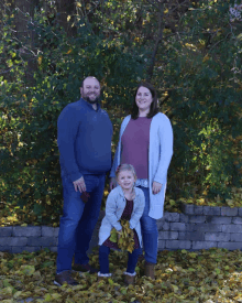 a family posing for a picture with a little girl holding a bunch of leaves