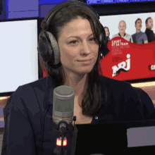 a woman wearing headphones stands in front of a microphone with a sign in the background that says " caout et sa team "