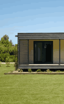 a small house with a porch and sliding glass doors sits in the middle of a lush green field