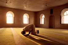 a man is praying in a mosque with the sun shining through the window .