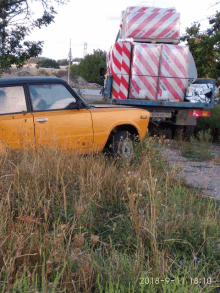 a yellow car is parked in a field next to a truck with a stack of boxes on the back