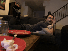 a man is laying on a couch with a plate of food on the table