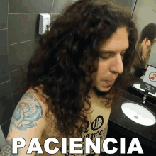 a man with long curly hair is standing in front of a bathroom sink with the word paciencia above him