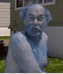 a naked man with blue hair and beard is sitting in front of a house