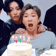 a group of young men are posing for a picture in front of a cake with candles on it .