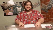 a man in a hawaiian shirt is sitting at a desk in front of a sign that says ' silly system '