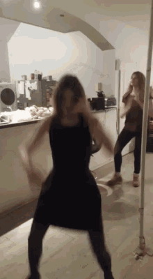 a woman in a black dress is dancing in front of a mirror in a kitchen