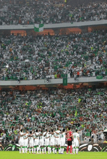 a group of soccer players stand on a field in front of a crowd wearing white jerseys