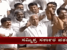 a group of men are raising their hands in the air in front of a sign that says ' kannada ' on it