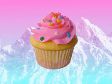 a cupcake with pink frosting and sprinkles in front of mountains