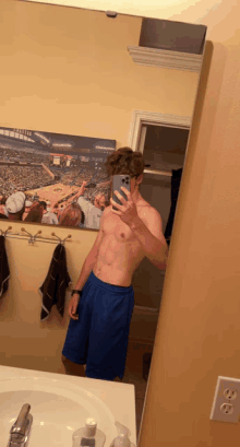 a shirtless man taking a selfie in front of a mirror with a picture of a stadium behind him