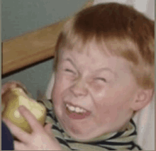 a young boy making a face while holding an apple