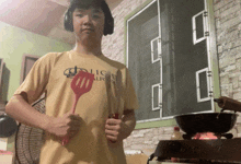 a man wearing headphones holds a red spatula in front of a stove top