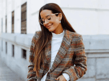 a woman wearing glasses and a plaid coat smiles