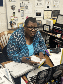 a woman sits at a desk in front of a wall that says lesley university on it