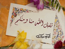 a card with arabic writing is sitting on top of a table next to flowers .