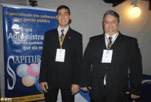 two men are standing in front of a banner that says " apitur "