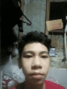 a young man in a red shirt takes a selfie in front of a wire fence