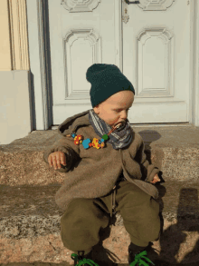 a little boy wearing a green beanie and green pants sits on a set of steps