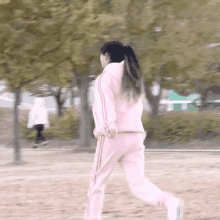 a woman in a pink hoodie and pink sweatpants is running in a park