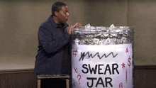 a man is standing next to a jar filled with money and a sign that says `` swear jar '' .