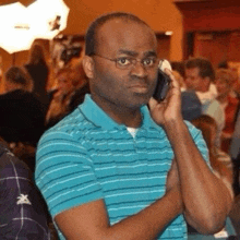 a man wearing glasses and a blue striped shirt is talking on a cell phone