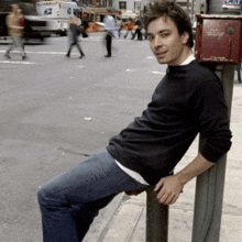 a man leans against a pole with a red box on it that says ' emergency ' on it