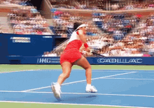 a woman in a red dress is playing tennis on a court with an ad for cadillac express in the background