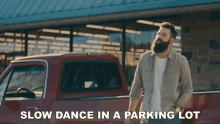 a man with a beard is standing in front of a red truck with the words slow dance in a parking lot written below him